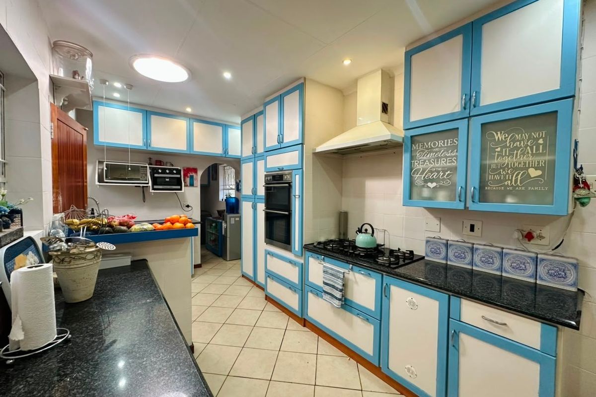A functional kitchen featuring blue and white cabinetry, granite countertops, a gas hob with extractor fan, and a built-in double oven.