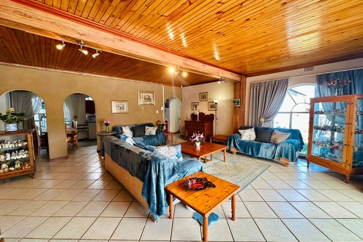 Spacious living area featuring a warm timber tongue and groove ceiling, exposed beams, ceramic tiled flooring, and distinctive arched doorways leading to adjacent rooms.
