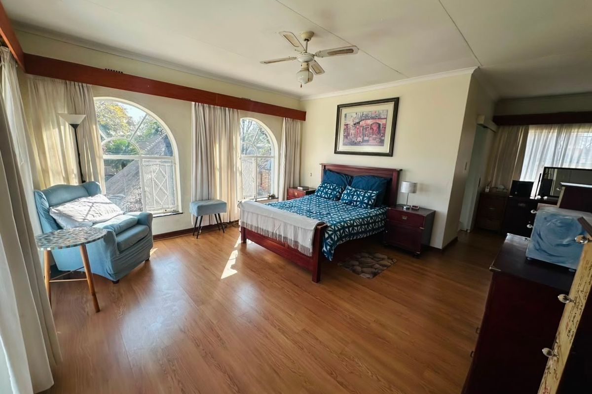 Spacious bedroom featuring laminate flooring, arched windows with timber pelmets, and a ceiling fan, offering a comfortable and well-lit living space.
