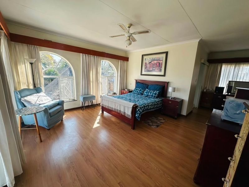 Spacious bedroom featuring laminate flooring, arched windows with timber pelmets, and a ceiling fan, offering a comfortable and well-lit living space.