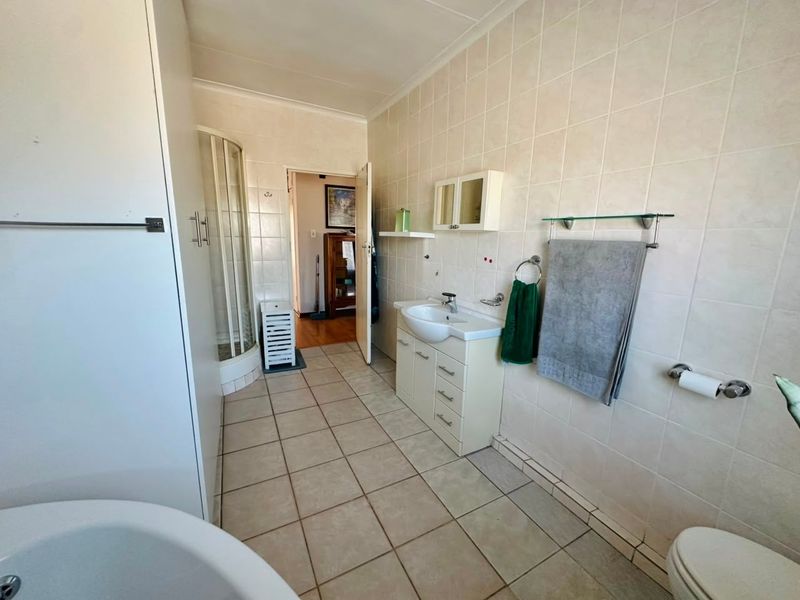 A functional bathroom featuring a shower enclosure, vanity unit with basin, toilet, and neutral wall and floor tiling.