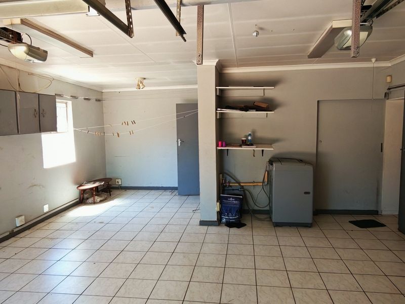 Spacious garage featuring tiled flooring, built-in wall cabinetry, and dedicated plumbing connections, offering versatile utility space with potential for workshop or storage use.