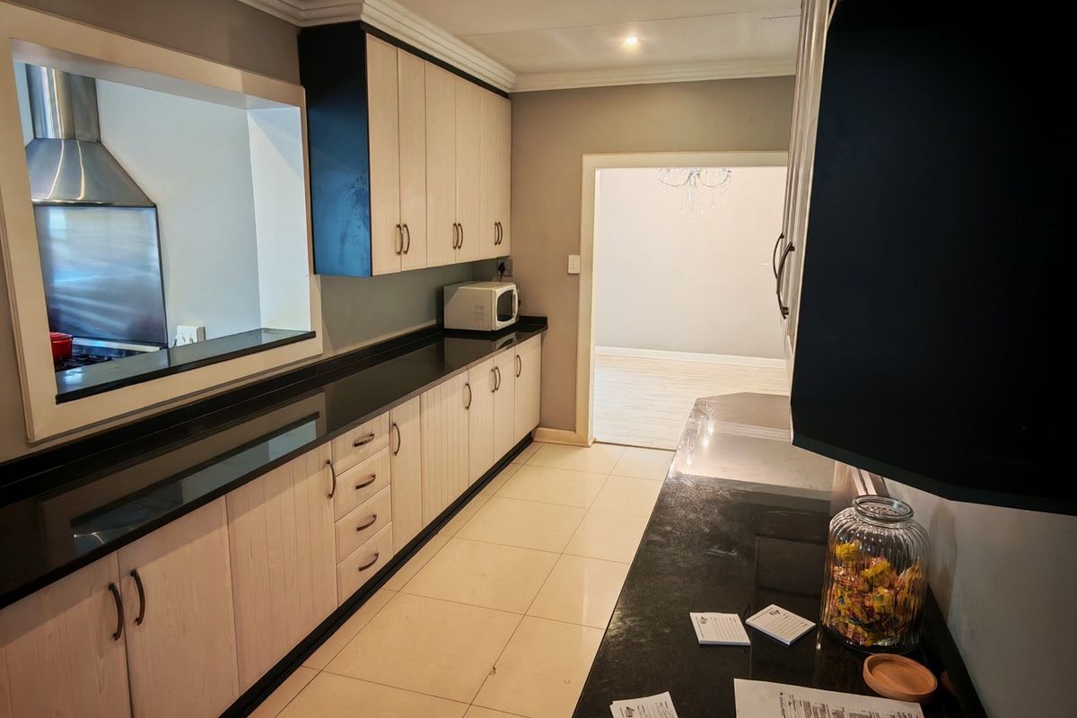 A functional kitchen featuring light wood-finish cabinetry, contrasting black granite countertops, tiled flooring, and a convenient pass-through window to the adjacent living area.