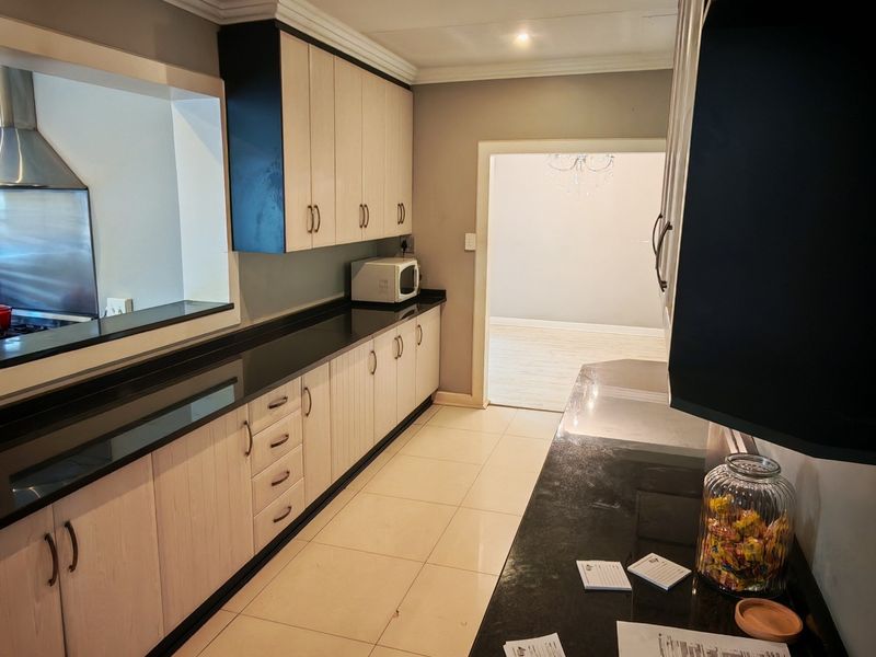 A functional kitchen featuring light wood-finish cabinetry, contrasting black granite countertops, tiled flooring, and a convenient pass-through window to the adjacent living area.