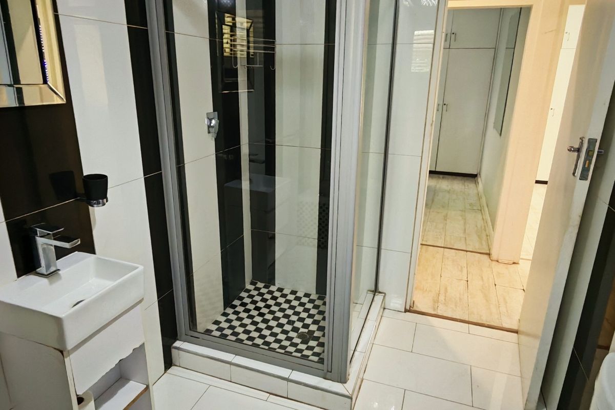 A modern bathroom featuring a glass shower enclosure, wall-mounted basin with mixer tap, and high-contrast black and white tiled finishes.