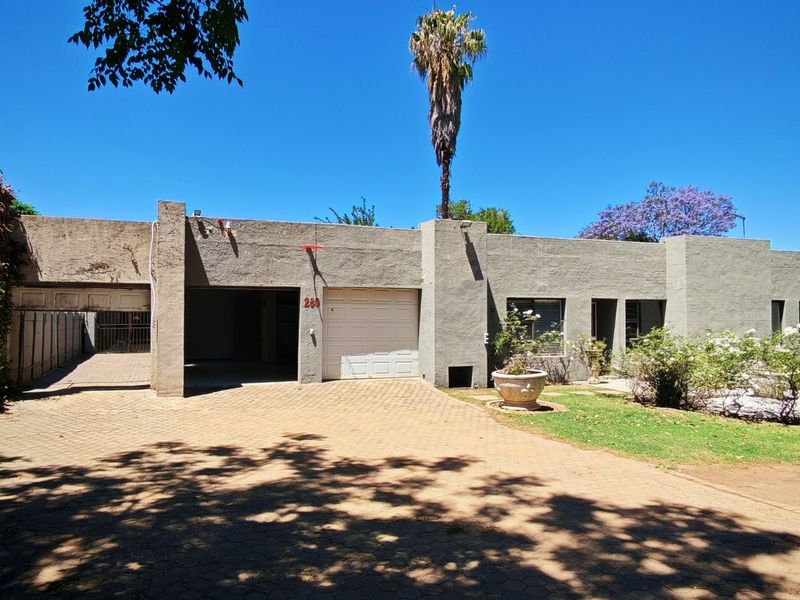 Front elevation of a single-story house featuring a paved driveway, double garage, carport, and established garden area.