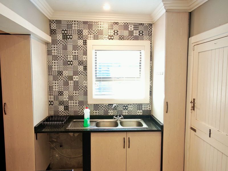 A functional scullery area featuring a double sink, patterned tile backsplash, and built-in cabinetry, providing a dedicated space for utility and wash-up tasks.
