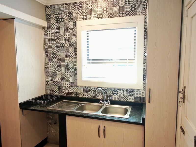 A functional scullery area featuring light wood-look cabinetry, a double stainless steel sink, and a decorative patterned tile splashback.