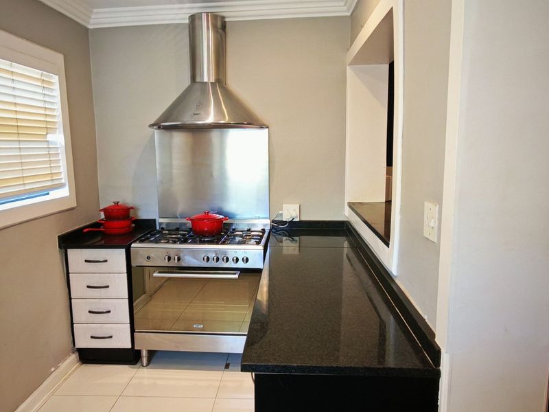 A functional kitchen featuring granite countertops, a stainless steel gas stove with extractor fan, and built-in cabinetry with tiled flooring.