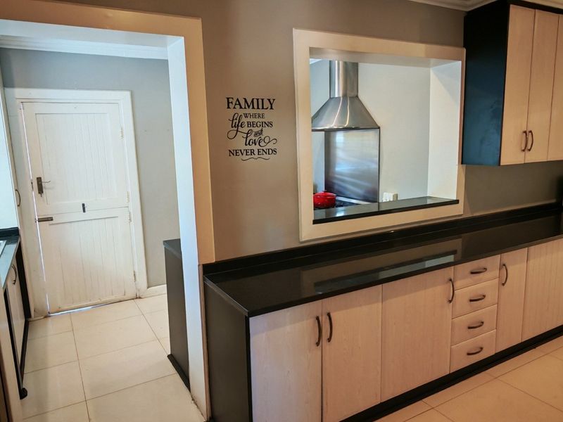 A functional kitchen featuring light wood cabinetry, dark granite countertops, tiled flooring, and a convenient pass-through window connecting to the adjacent space.
