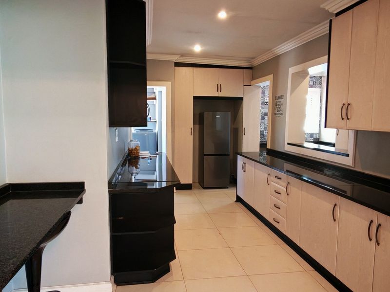 A functional kitchen featuring light wood cabinetry, contrasting black granite countertops, tiled flooring, and recessed lighting, with a clean and well-maintained layout.