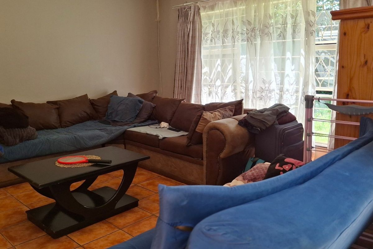 A living room area featuring tiled flooring and large windows with security gates, providing natural light to the space.