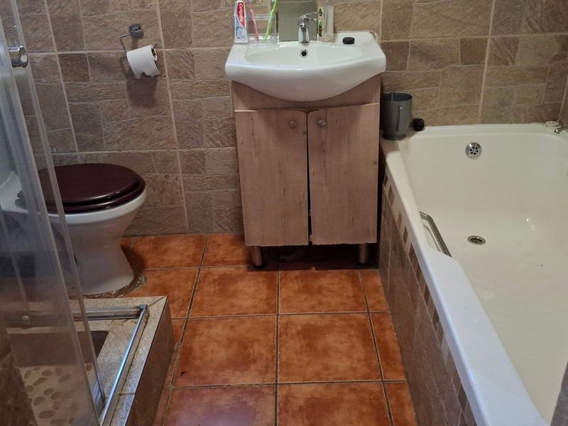 Compact bathroom featuring a bathtub, shower enclosure, toilet, and vanity cabinet with tiled wall and floor finishes.