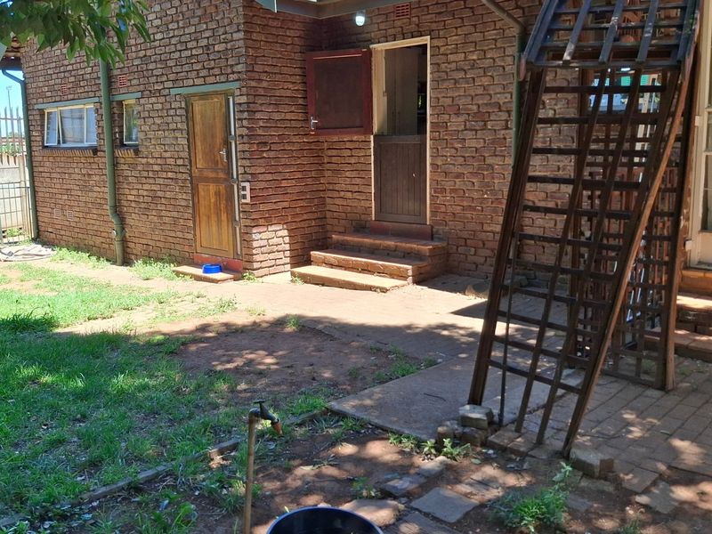 Rear exterior view of a brick house featuring a paved patio area, external staircase, and access to the garden.