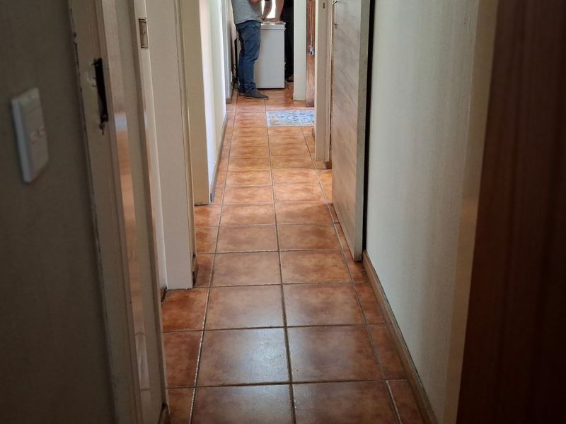 A narrow residential hallway featuring terracotta-style ceramic floor tiles and multiple internal door access points.