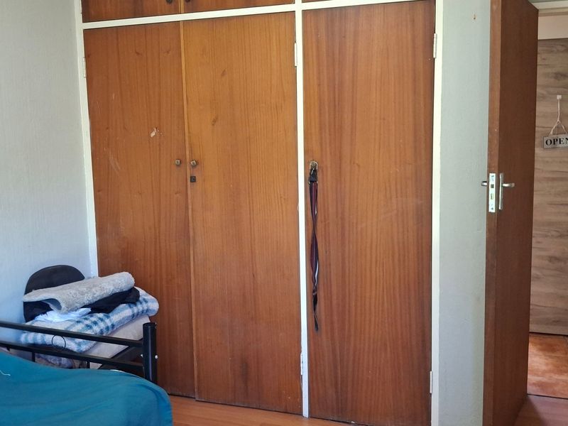 Bedroom featuring built-in wooden cupboards and laminate flooring, showing signs of wear and tear on the cabinetry.
