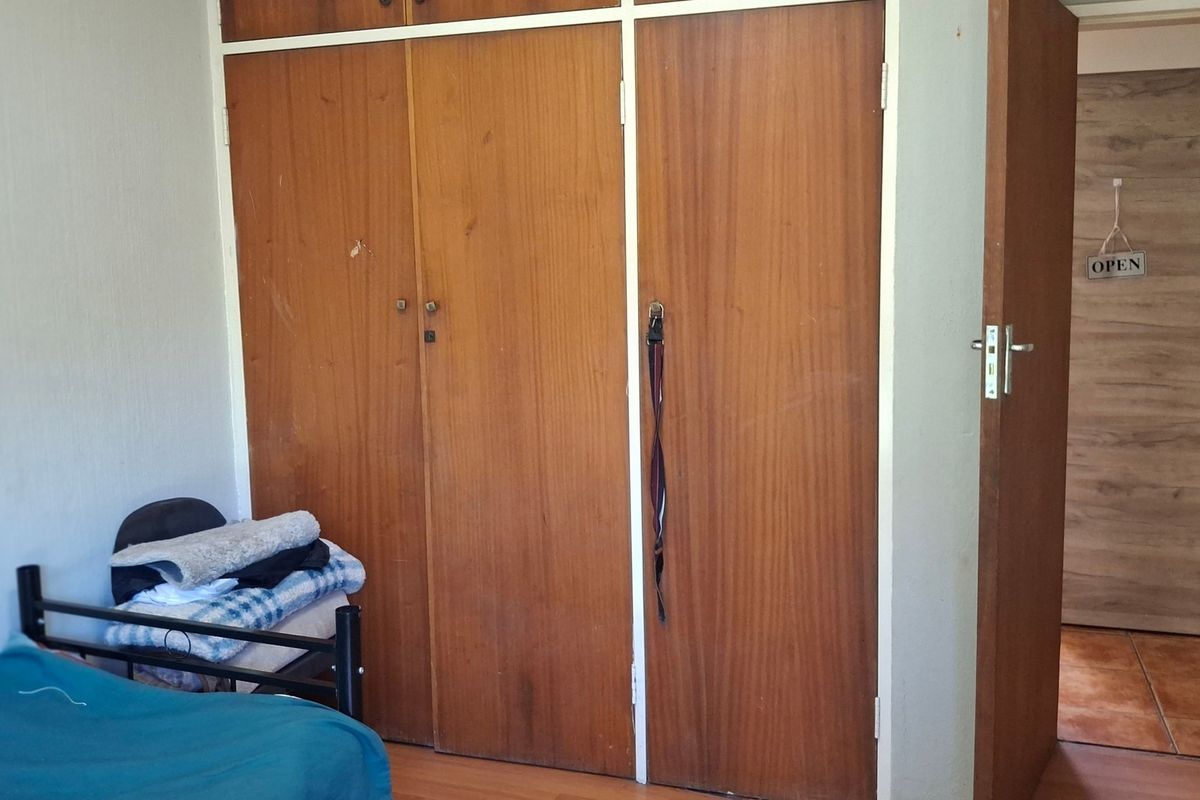 Bedroom featuring built-in wooden cupboards and laminate flooring, showing signs of wear and tear on the cabinetry.