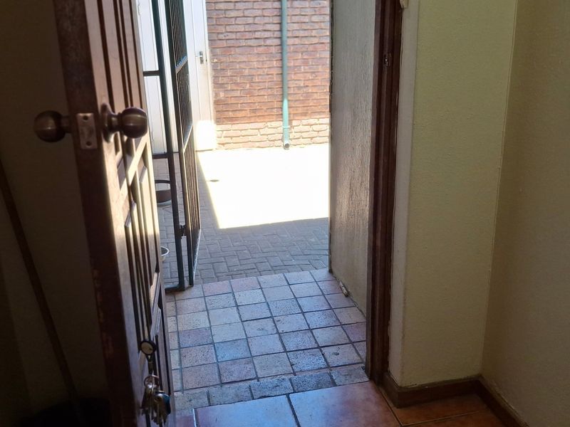 An interior entry area featuring tiled flooring and a timber door leading out to a paved courtyard with a security gate.