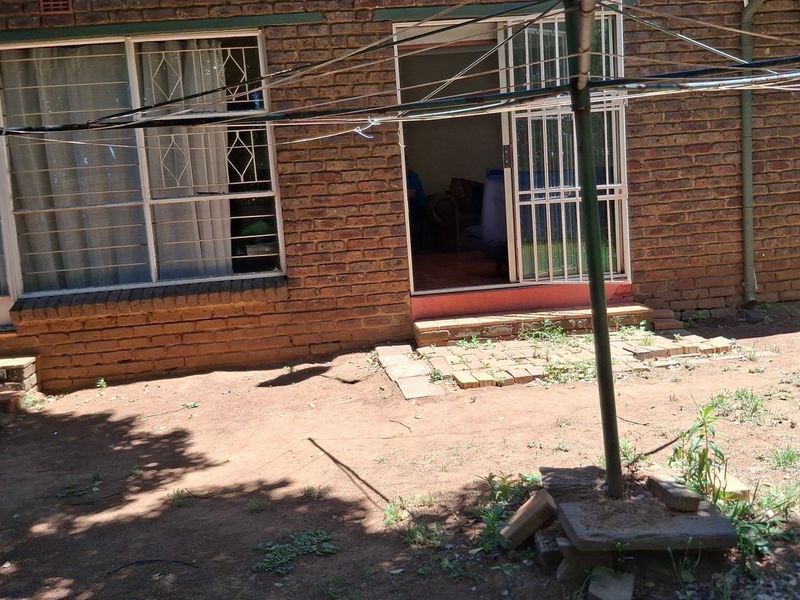 Rear exterior view of a face brick house featuring security bars, a sliding door entrance, and an unlandscaped garden area.