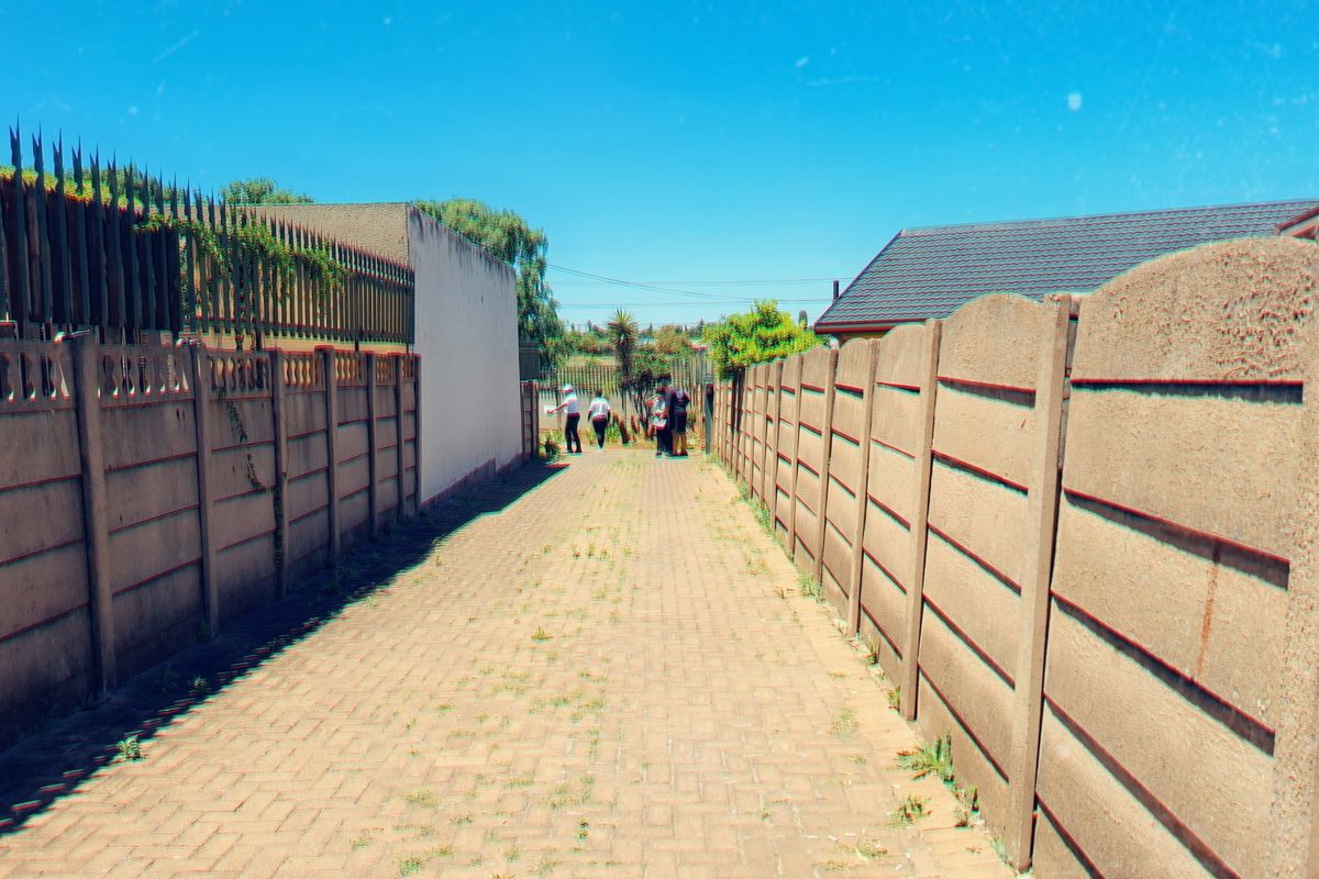 A narrow paved pathway enclosed by precast concrete boundary walls and topped with metal security spikes.