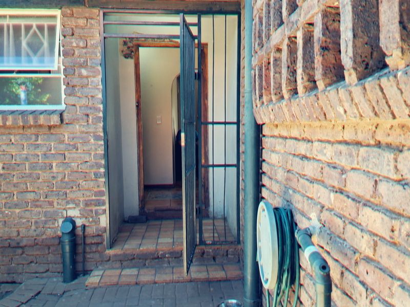 Rear exterior view showing a brick facade, security gate entrance, and tiled threshold area with visible signs of wear.