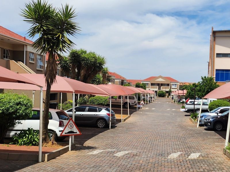 A view of the townhouse complex driveway featuring paved surfaces and multiple covered parking bays with shade cloth structures.