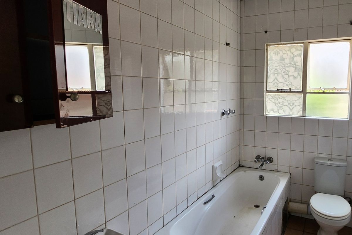 A dated bathroom featuring white wall tiles, a standard bathtub, and a toilet, requiring cosmetic updates to modernize the space.