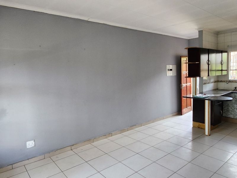 An open-plan living and kitchen area featuring tiled flooring, built-in cabinetry, and a breakfast bar, offering a blank canvas for renovation.
