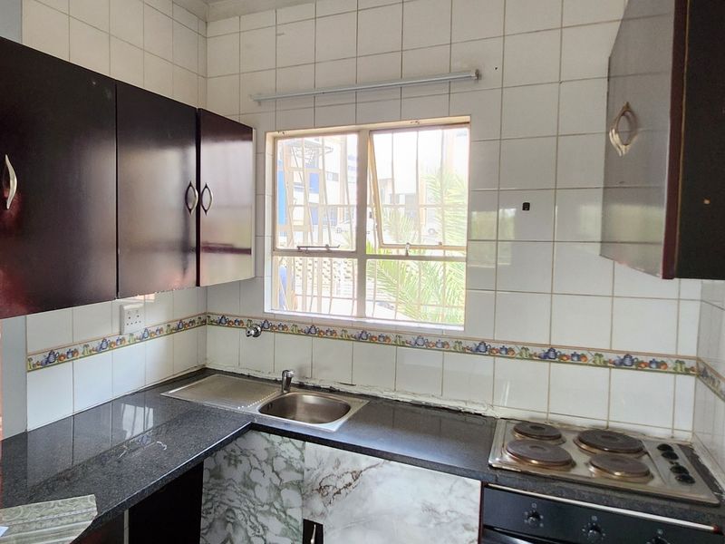 A functional kitchen featuring dark cabinetry, granite countertops, a built-in electric hob and oven, and tiled splashbacks with a window for natural light.