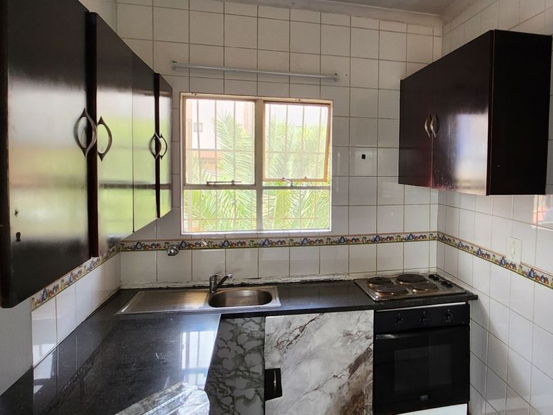 A compact kitchen featuring dark cabinetry, granite countertops, a built-in oven and hob, and tiled walls with a decorative border.