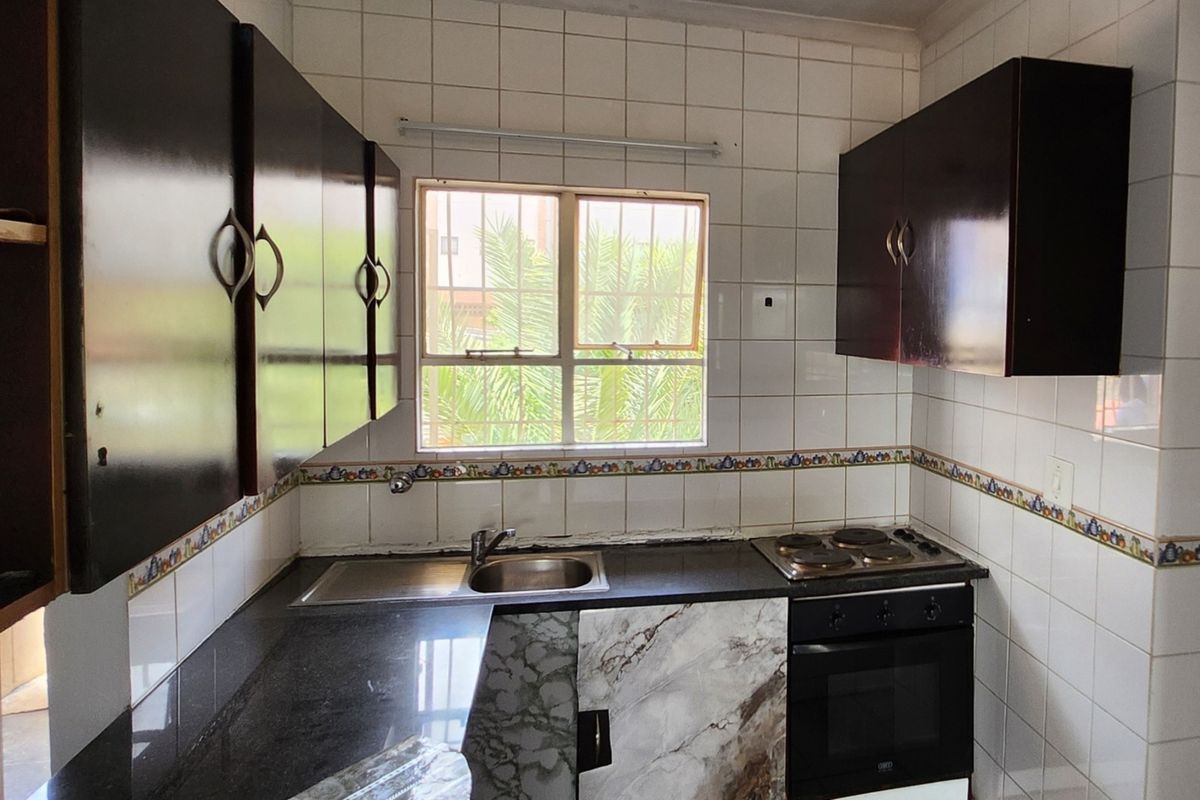 A compact kitchen featuring dark cabinetry, granite countertops, a built-in oven and hob, and tiled walls with a decorative border.