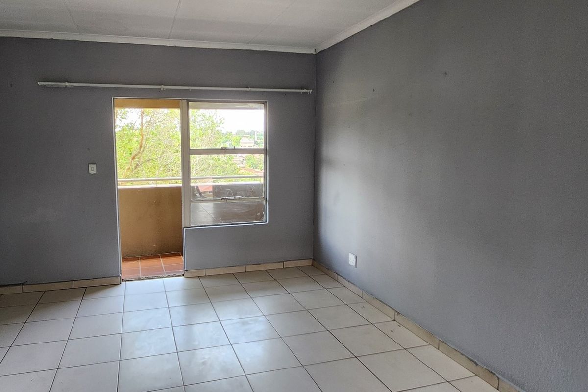 An empty bedroom featuring tiled flooring and a sliding door leading to a balcony, providing natural light and access to outdoor space.