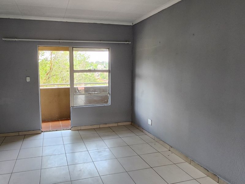 An empty bedroom featuring tiled flooring and a sliding door leading to a balcony, providing natural light and access to outdoor space.