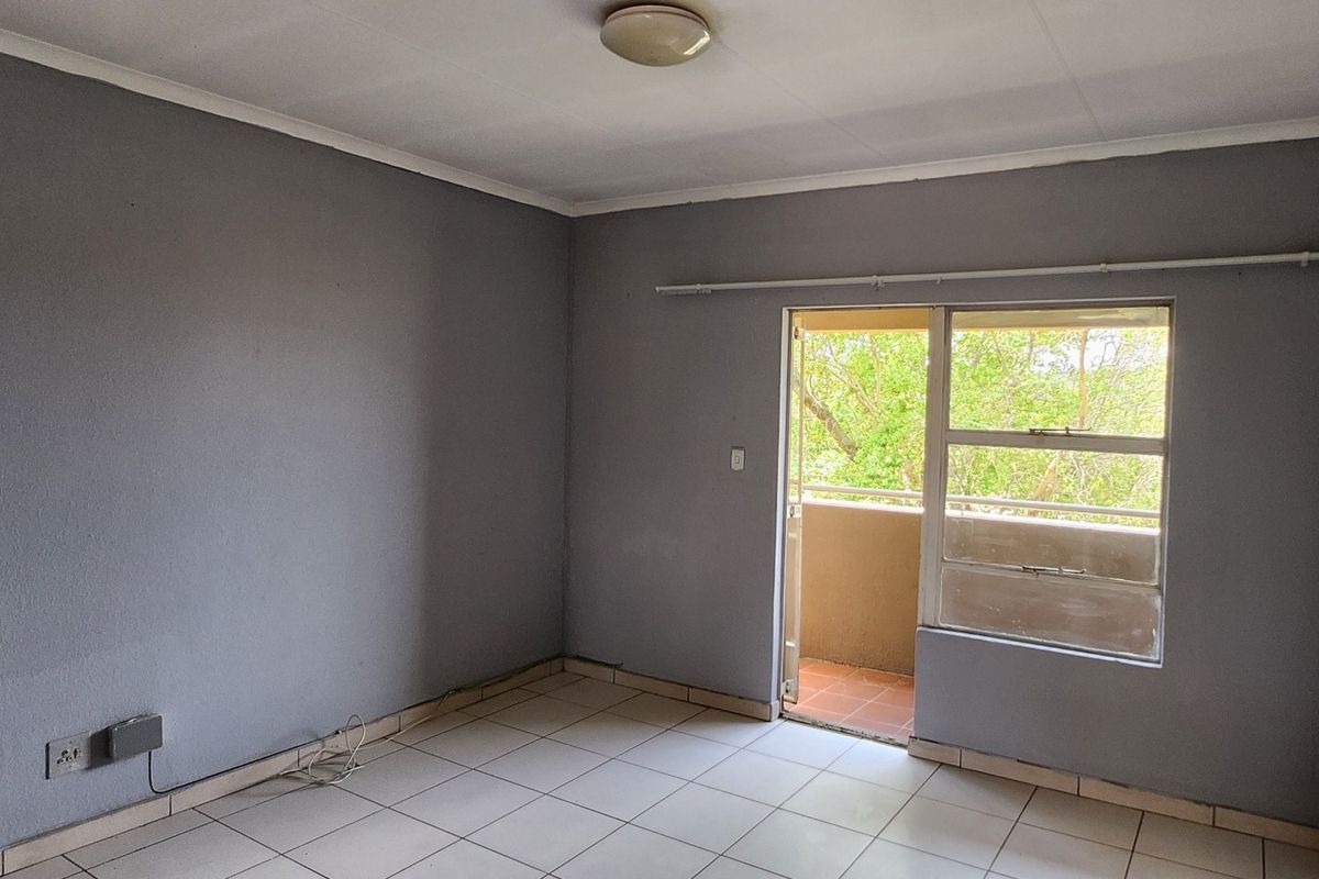 An empty living room featuring tiled flooring and direct access to a balcony through a sliding door.