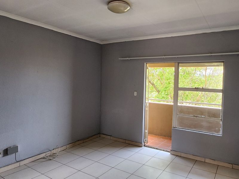An empty living room featuring tiled flooring and direct access to a balcony through a sliding door.