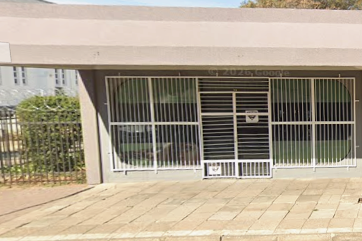 Front exterior view of an office building featuring a concrete overhang, security bars on windows, and paved entrance area.