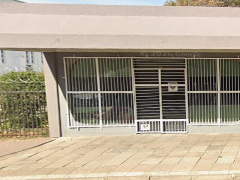 Front exterior view of an office building featuring a concrete overhang, security bars on windows, and paved entrance area.