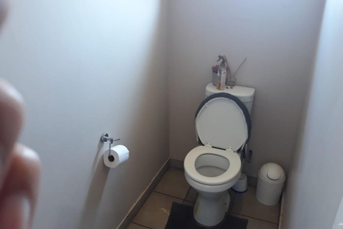 A compact office restroom featuring a standard white toilet and wall-mounted toilet paper holder with tiled flooring.