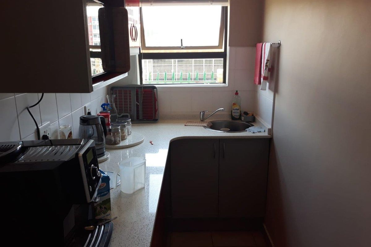 Compact kitchenette featuring built-in cabinetry, a stainless steel sink, tiled splashbacks, and a window providing natural light.