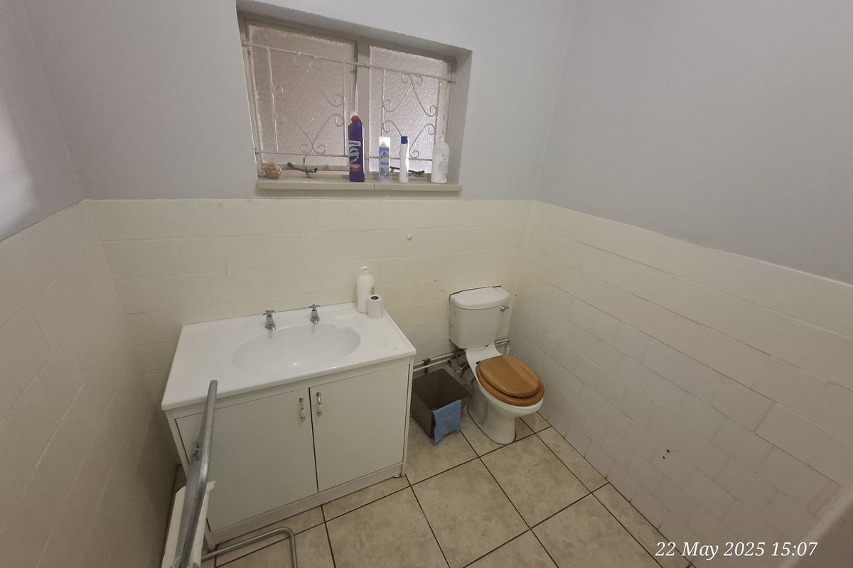 A functional bathroom featuring a vanity basin, toilet, and tiled walls with a security-grilled window.