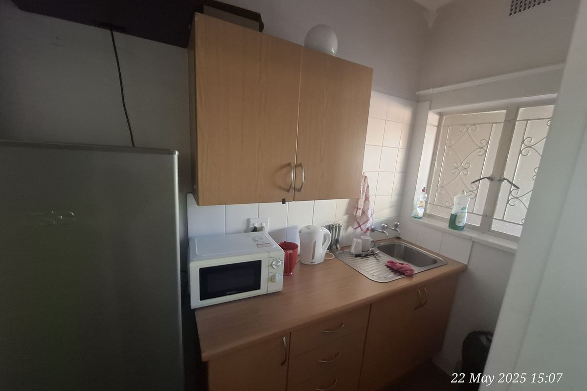 Compact kitchenette featuring wooden cabinetry, a stainless steel sink, and tiled splashback, providing essential prep space for a small office or utility area.