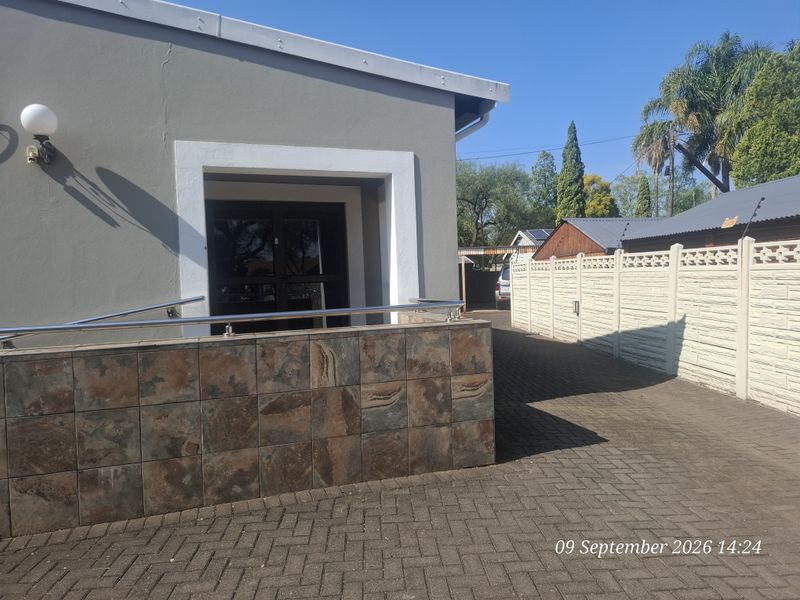 Exterior view of the office entrance featuring a paved driveway, tiled retaining wall with a stainless steel handrail, and a secure boundary wall.