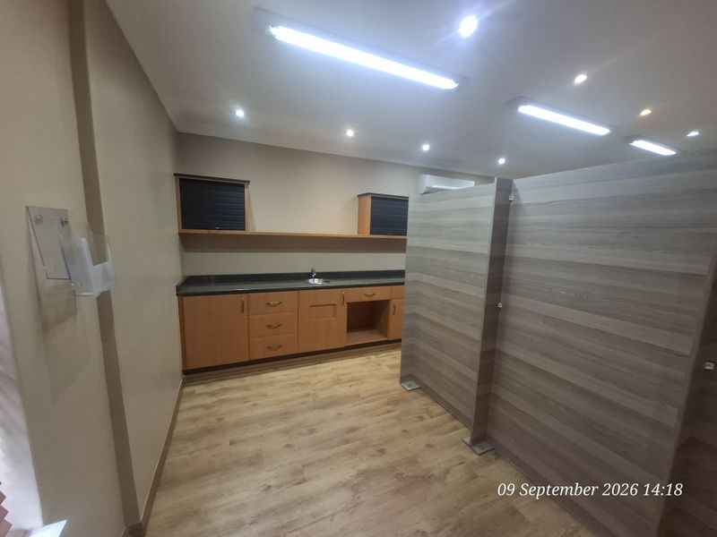A functional office kitchenette featuring built-in wooden cabinetry, a sink, and durable laminate flooring, partitioned for privacy within the workspace.