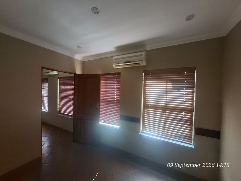 A bright, empty office space featuring tiled flooring, recessed downlights, split-system air conditioning, and wooden venetian blinds.