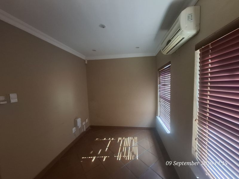 A vacant office space featuring tiled flooring, recessed lighting, a wall-mounted air conditioning unit, and venetian blinds on the windows.