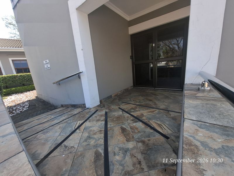 Accessible office entrance featuring a tiled ramp with stainless steel handrails and a glass door entry.
