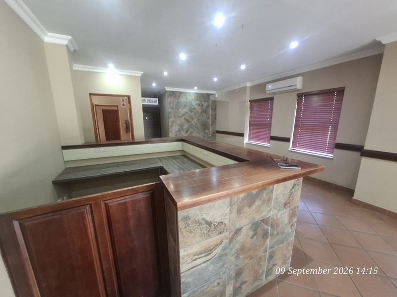 Spacious office area featuring a built-in reception desk with stone cladding, recessed lighting, split-system air conditioning, and tiled flooring.