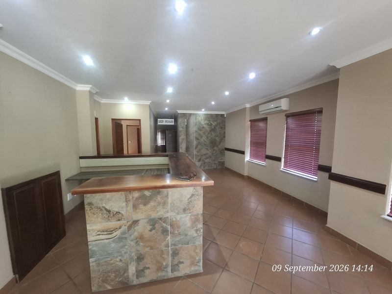 Spacious office area featuring a built-in reception desk with stone cladding, ceramic tiled flooring, recessed lighting, and air conditioning.