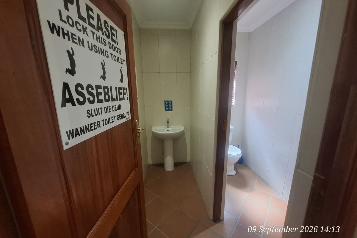 A functional office bathroom featuring a pedestal basin and a separate toilet cubicle with tiled flooring and walls.