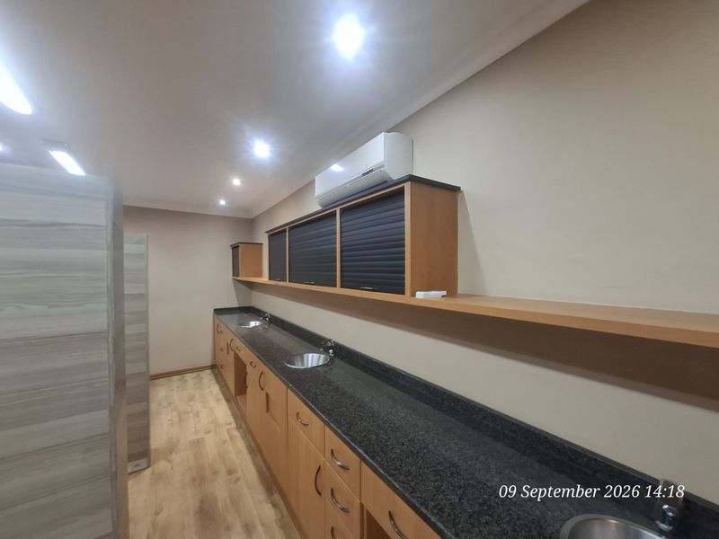 A clean, modern office kitchenette area featuring extensive built-in cabinetry, granite countertops with multiple integrated sinks, and wall-mounted air conditioning.